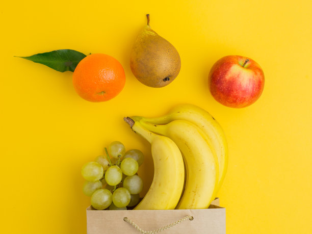 不同健康食品的纸袋以黄色为背景。前视图。平的。一个装着水果的棕色纸袋图片下载