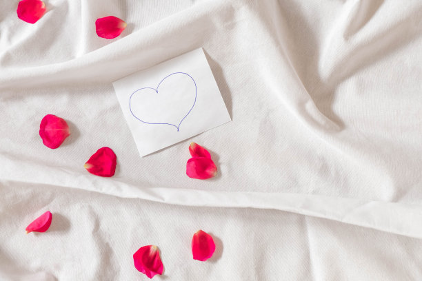 白色的床单上有粉红色的玫瑰花瓣，上面有手写的心图片下载