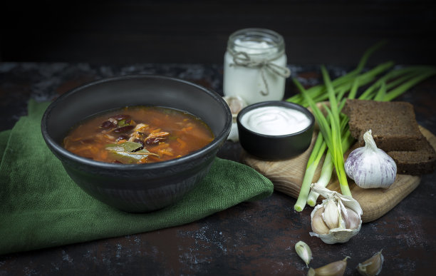 红罗宋汤，乌克兰的传统民族菜肴在库存照片上，罗宋汤被盛在黑陶里，配上酸奶油、大葱和大蒜，背景是深色的，用绿色的纺织品做的。图片下载