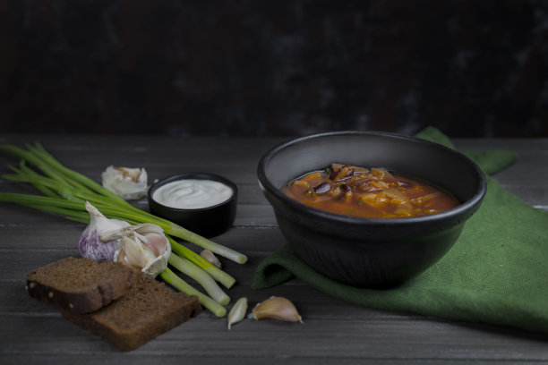 红罗宋汤，乌克兰的传统民族菜肴在库存照片上，罗宋汤盛在黑陶里，配上酸奶油、大葱和大蒜，背景是深色的木质材料，用绿色纺织品制成。复制spase图片下载