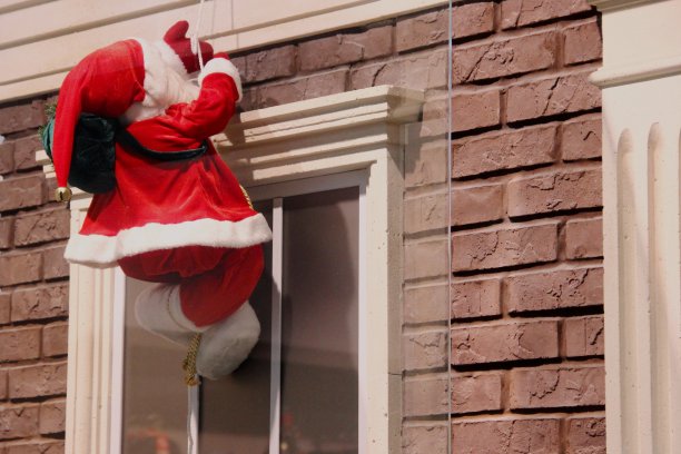 圣诞老人的正面装饰是一根绳子。圣诞老人爬上烟囱，背对着窗户和房子砖立面的背景图片下载