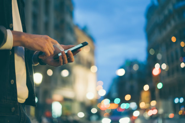 这是一个男性手拿智能手机的特写照片，晚上在城市街道上，搜索互联网或社交网络，嬉皮士在聊天中输入短信或消息图片下载