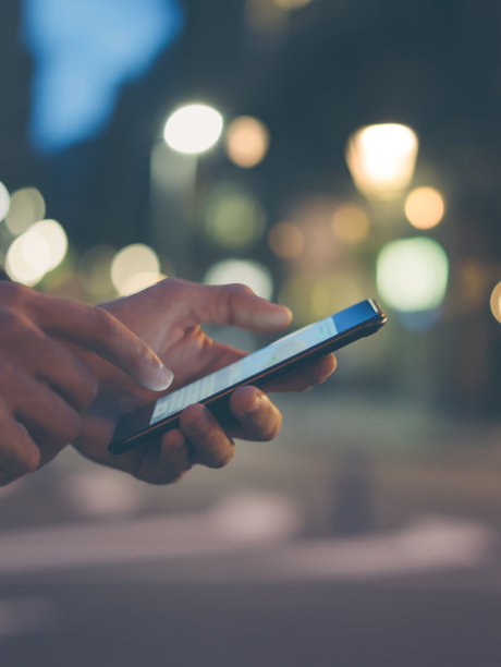 这是一个男性手拿智能手机的特写照片，晚上在城市街道上，搜索互联网或社交网络，嬉皮士在聊天中输入短信或消息图片下载