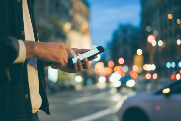 这是一个男性手拿智能手机的特写照片，晚上在城市街道上，搜索互联网或社交网络，嬉皮士在聊天中输入短信或消息图片下载