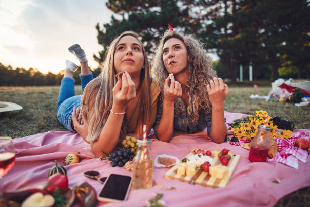 可爱的年轻女子一边吃零食，一边放松在野餐毯子上图片下载