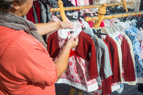 一位年长的妇女，一位白发苍苍的祖母，正在为她的孙子挑选一件衣服。她周围有很多风格和颜色。消费主义的概念图片下载