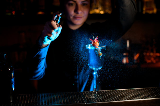 专业的调酒女往玻璃杯里的鸡尾酒上喷洒着掉落的浆果和花，还有苦味图片下载