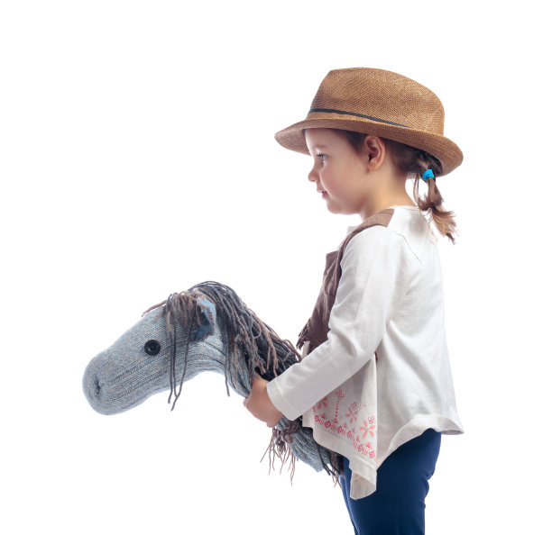 可爱的小女孩打扮得像个牛仔在玩自制的马。图片下载