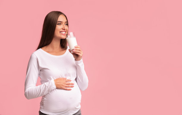 欢快的孕妇饮用天然牛奶站在粉红色的背景图片下载