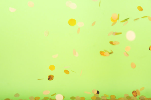 金色的五彩纸屑飘落在醒目的霓虹绿色背景上，节日庆典的背景图片下载