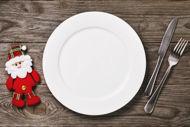 空的白色盘子和餐具与玩具圣诞老人在一个木制的桌子上，俯视图。食品的背景图片下载