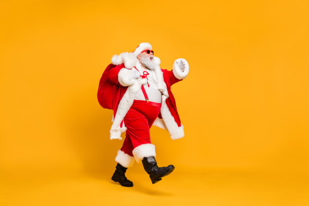 丰满的身材侧面照片时髦的胖圣诞老人与巨大的腹部拿着礼物愿望包去走旅行在圣诞夜夜戴着圣诞帽吊带孤立明亮的颜色背景图片下载