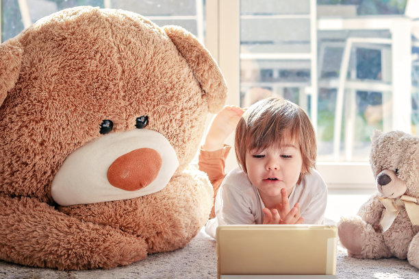 可爱的小孩躺在地板上看卡通片，家里还有两个玩具熊。现代的童年。图片下载