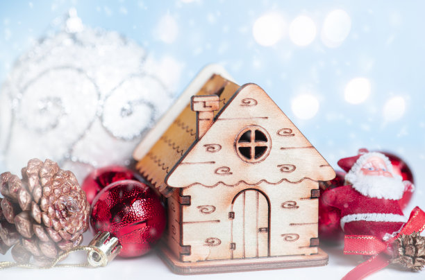 美丽的圣诞背景。小玩具屋，红色的圣诞玻璃球，松果，在闪闪发光的背景上。图片下载