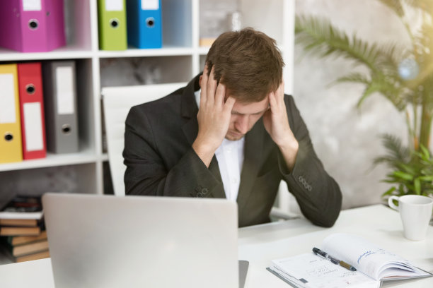 帅哥经理在一天结束的时候坐在办公室里工作，感觉又累又烦。多任务、工作概念图片下载