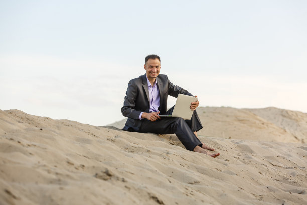 在沙漠中使用笔记本电脑和手机的商人图片下载