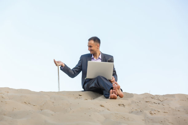在沙漠中使用笔记本电脑和手机的商人图片下载