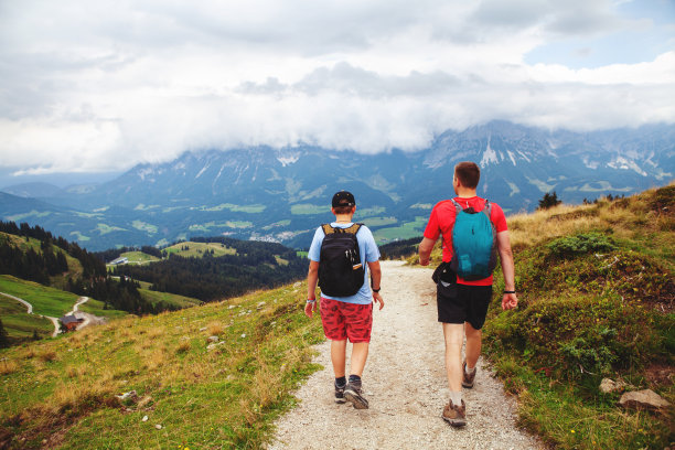 一个父亲和十几岁的儿子走在阿尔卑斯山高的人行道上，奥地利，而在他们的徒步旅行与美丽的全景和山脉在远处。图片下载