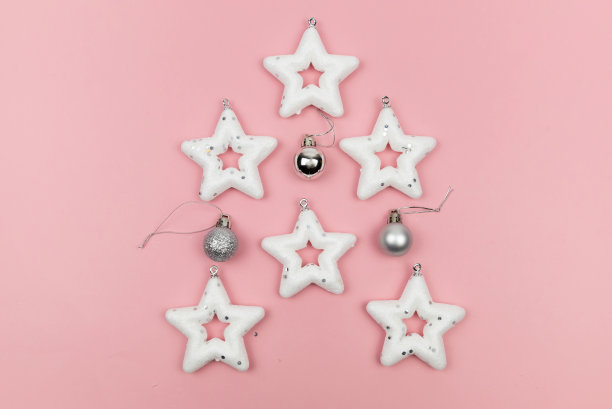 节日装饰。由白色星星、圣诞树玩具和粉色背景上的银球组成的创意作品。顶视图,特写镜头。图片下载