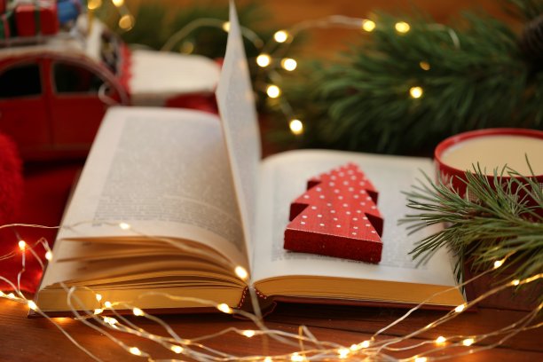 冬天的舒适的读书。关于圣诞节的书籍。打开书装饰红色圣诞树，咖啡杯，冷杉树枝和圣诞装饰在红色的木制背景。冬天的书和茶图片下载
