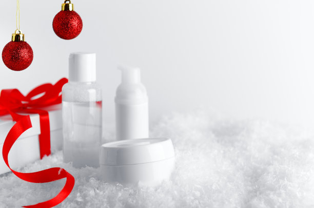 护肤化妆品瓶在程式化的雪覆盖表面。白色礼盒与红色丝带和闪闪发光的小装饰品背景。新年和圣诞节女性礼物创意图片下载