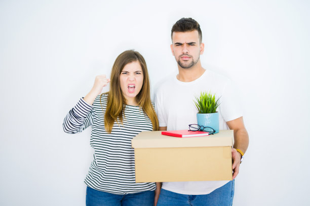 年轻的夫妇抱着纸箱搬到一个新的家在白色孤立的背景恼怒和沮丧的大喊与愤怒，疯狂的大喊与举手，愤怒的概念图片下载