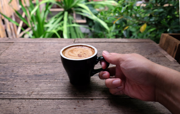 热咖啡杯放在木桌上，以花园为自然背景，清晨雨天的种植园背景——意象图片下载