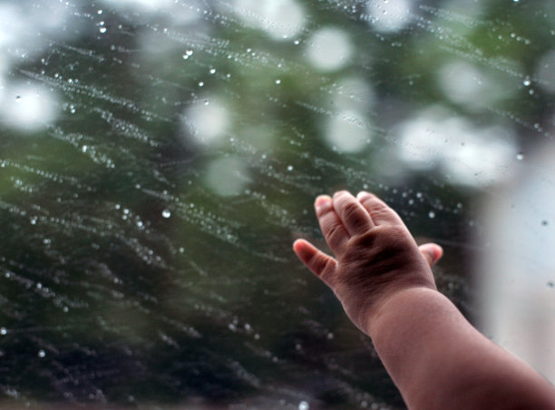 新生儿特写手。雨点落在玻璃窗上，以家在雨季抽象的背景，水滴落在玻璃上图片下载