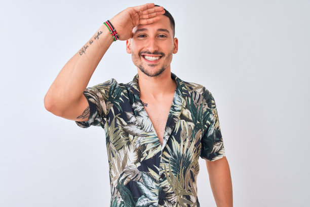 年轻英俊的男子穿着夏威夷夏装越过孤立的背景，非常高兴，微笑着看远与手在头上。搜索概念。图片下载