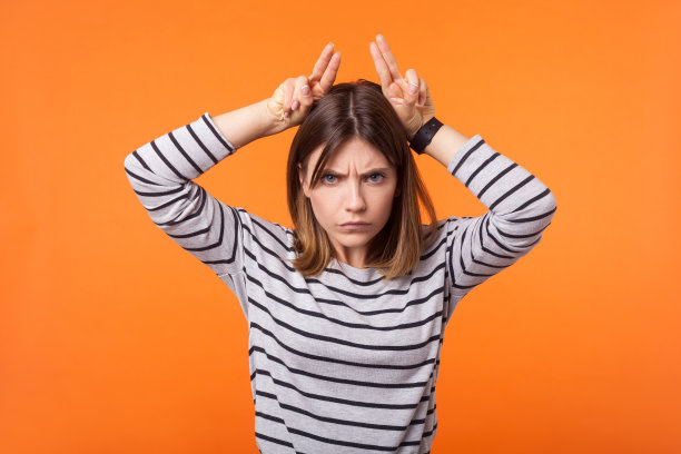 愤怒的年轻女子肖像与棕色头发在长袖条纹衬衫。室内工作室拍摄孤立的橙色背景图片下载