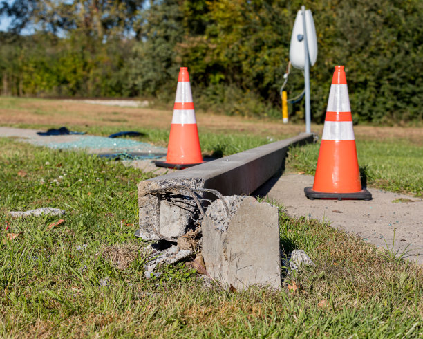 路面上的混凝土路灯因车祸损坏，电线外露，横放在人行道上。背景是橙色的交通锥和碎玻璃图片下载