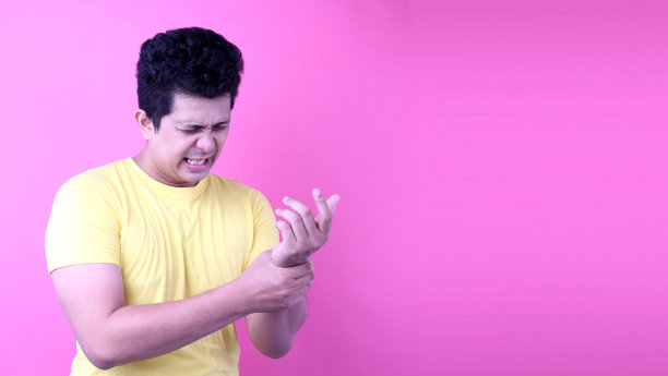 年轻的亚洲男子手腕疼痛在粉红色的背景在工作室与复制空间。图片下载