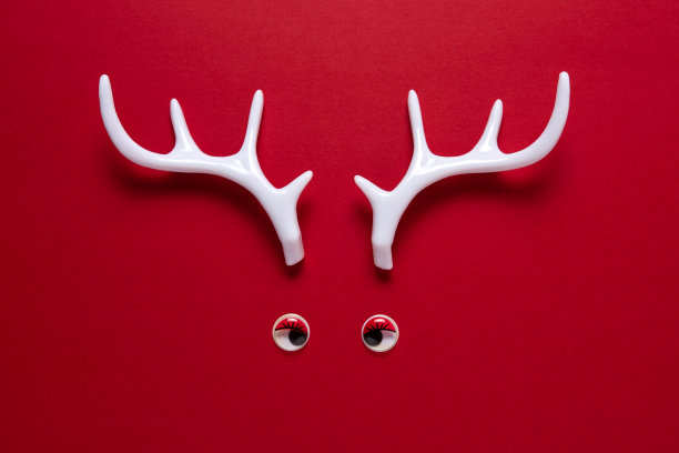 红色背景上的白色驯鹿角和玩具眼睛。最小的新年或圣诞节背景概念。图片下载