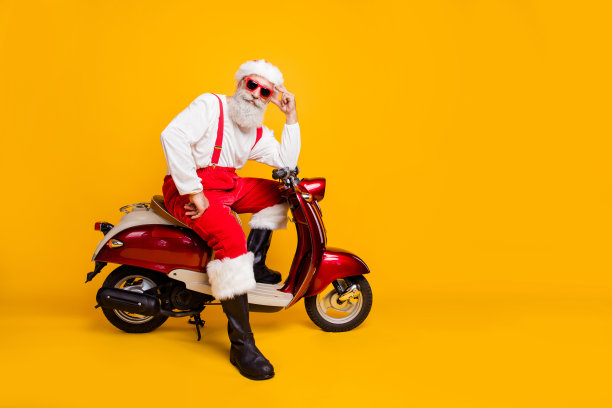全身照片有趣的圣诞老人在节日的心情准备圣诞主题派对坐在复古自行车穿太阳眼镜裤子帽子衬衫靴子孤立的黄色背景图片下载