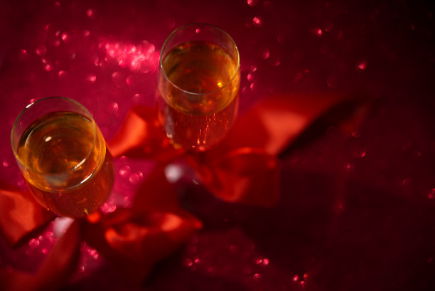 俯视图上的两杯香槟装饰红丝带在红色闪闪发光的背景。情人节或婚礼庆祝概念。副本的空间。软焦点图片下载
