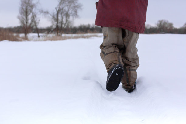 从一个穿着胶靴走在雪地上的男人的身后看到的景色图片下载