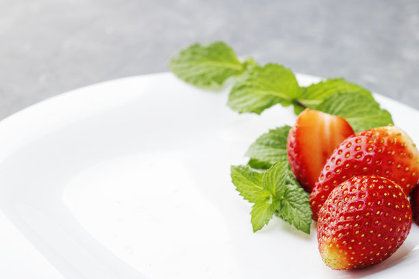 白色盘子上的新鲜草莓，蓝色背景上的薄荷叶。有选择性的重点。本空间图片下载