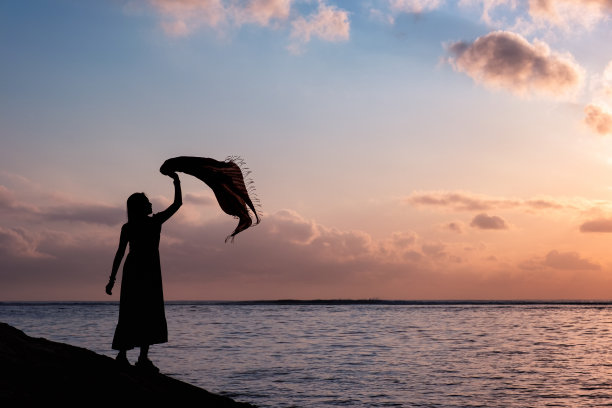 亚洲妇女放松与举起布在热带海洋与色彩斑斓的天空图片下载