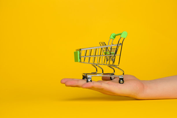 一个男人手里拿着一辆从超市买来的空金属手推车。物体在黄色背景上。水平的照片。交易的概念。图片下载