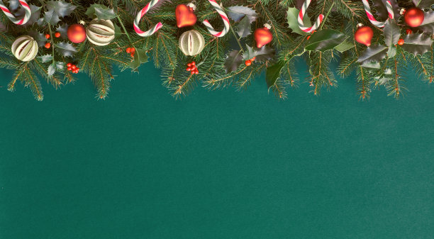 有创意的圣诞公寓铺在绿色的纸上，上面有红色的装饰，有足够的复制空间。用天然冷杉和冬青树枝装饰糖果手杖、玻璃小装饰品和干酸橙水果。图片下载