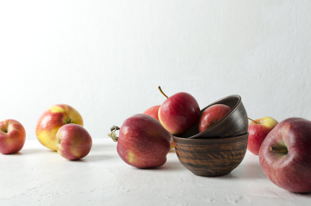 靠在明亮的墙上的白色桌子上，放着新鲜成熟的苹果，装满苹果的质朴的碗图片下载
