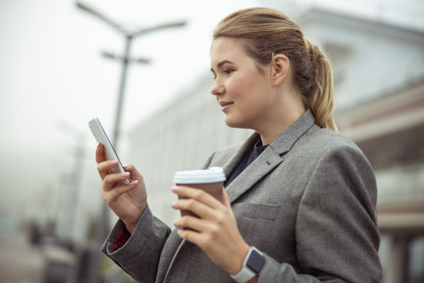 一位年轻漂亮的女士在街上用手机图片下载