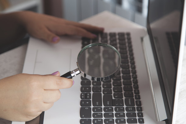 女人手持放大镜和电脑键盘图片下载