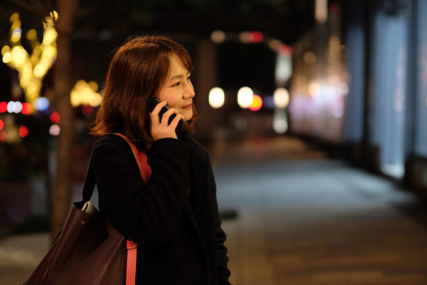 一名亚洲年轻女子晚上在户外打电话微笑。图片下载