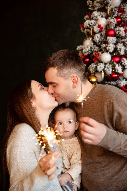 年轻漂亮的父母和刚出生的宝宝手拿烟花庆祝新年或圣诞节。全家福。图片下载