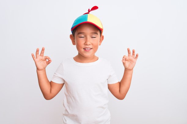 漂亮的孩子男孩戴着有趣的彩色帽子与螺旋桨在孤立的白色背景放松，微笑着闭上眼睛做冥想手势与手指。瑜伽的概念。图片下载