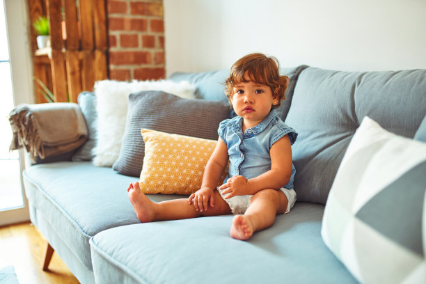 漂亮的蹒跚学步的小女孩穿着蓝色牛仔衬衫坐在沙发上图片下载