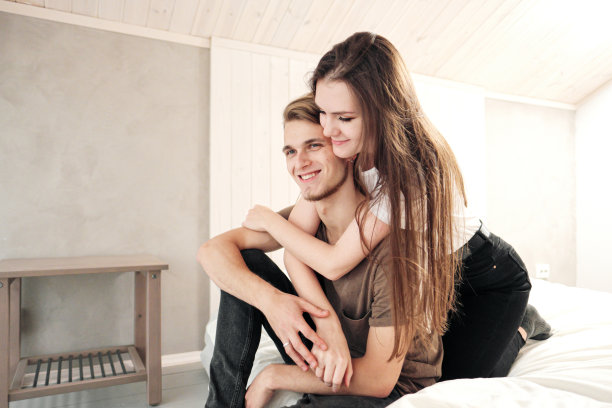 年轻夫妇，男人和女人在家里的卧室里。他们在床上打滚、嬉戏、打枕头、拥抱。家庭的夜晚。图片下载