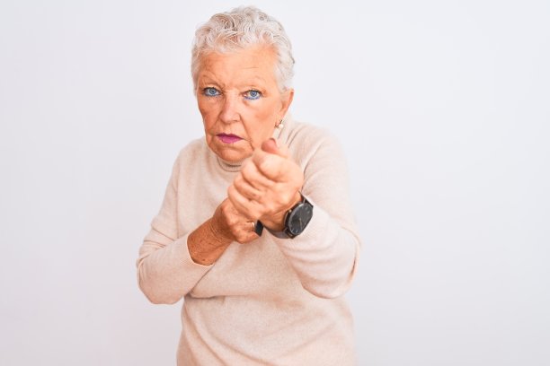 年长的白发女子穿着高领毛衣站在孤立的白色背景上，准备用拳头打拳的姿势，一脸愤怒和不安，怕出问题图片下载