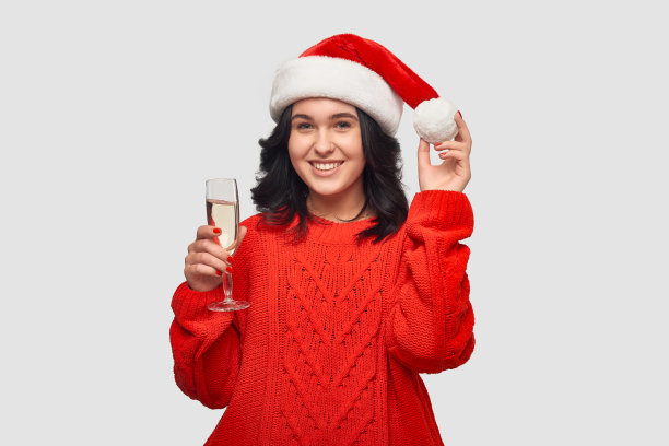 漂亮的黑发女孩穿着红毛衣戴着圣诞帽拿着香槟。图片下载